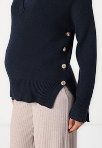 Navy knitted sweater with a V-neck, ribbed texture, and side buttons. Paired with light gray ribbed wide-leg pants.