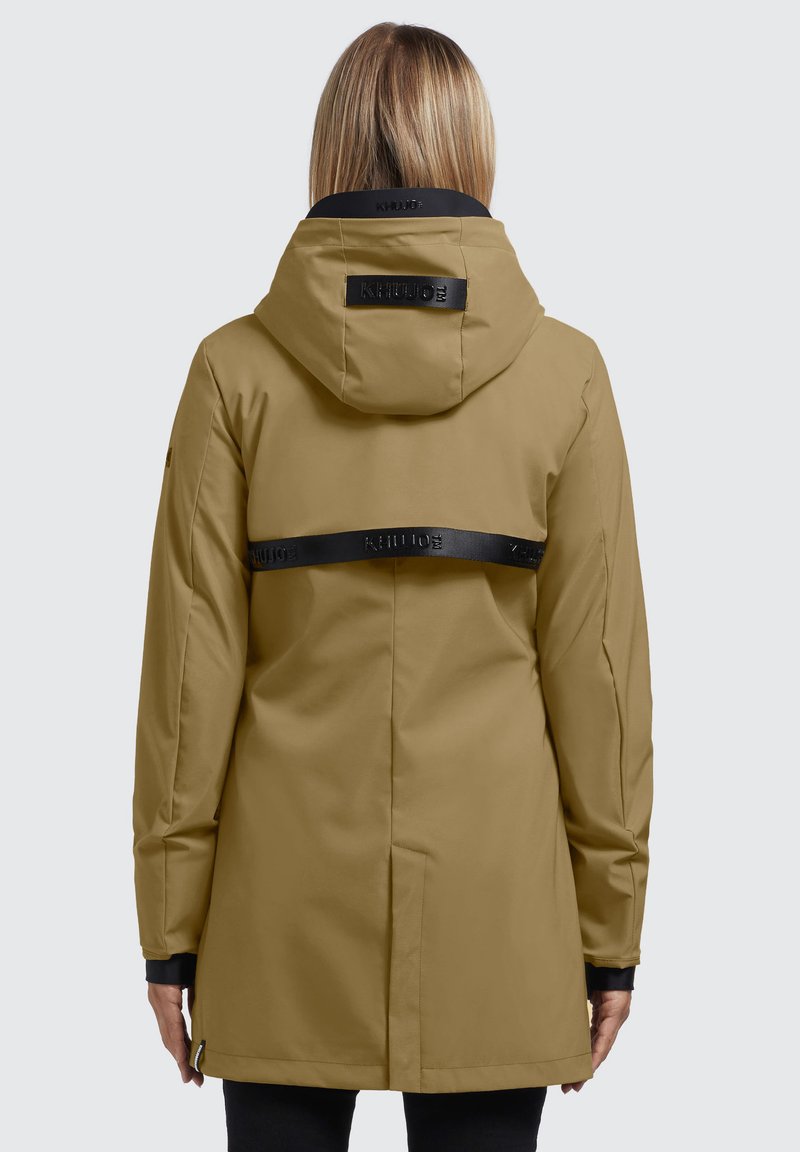 Veste imperméable beige avec une bordure noire à la capuche et une sangle dans le dos. Elle est dotée de longues manches et d'une coupe droite, idéale pour les activités en plein air.