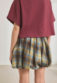 Korte mouwen maroon top met een losse pasvorm, gecombineerd met een blauw, geel en bruin geruit rokje met een geplooide design en elastische zoom.