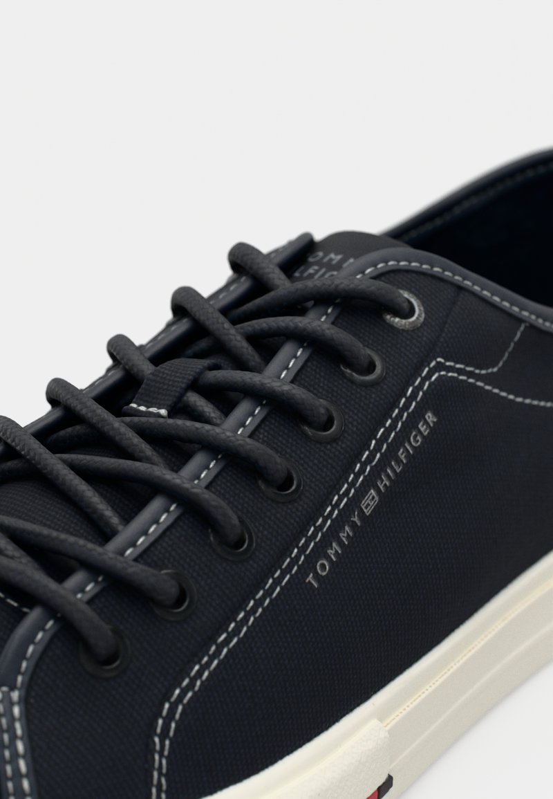 Baskets en toile marine avec des coutures blanches, lacets ronds et semelle en caoutchouc. Présente un logo imprimé sur le côté. Les accents incluent un dessus texturé.