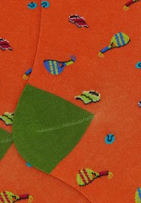 Calzini arancioni con un risvolto verde, decorati con un motivo giocoso di maracas e forme colorate. Il materiale sembra lavorato a maglia con una texture liscia.