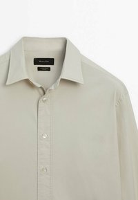 Jasno beżowa koszula z długim rękawem zapinana na guziki, wykonana z bawełny z elastanem. Posiada klasyczny kołnierzyk oraz pięć przezroczystych guzików wzdłuż listwy.