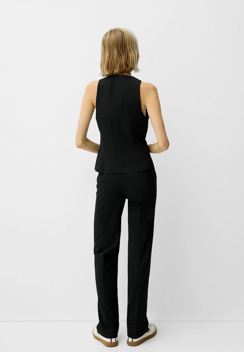 Top negro sin mangas con un diseño ajustado, combinado con pantalones negros a medida y zapatillas blancas. El tejido parece suave con una silueta estructurada.