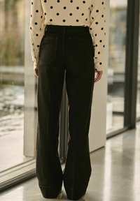 Pantalons larges noirs en tissu résistant, dotés de deux poches arrière et d'une taille haute. Agrémentés d'un ourlet soigné.