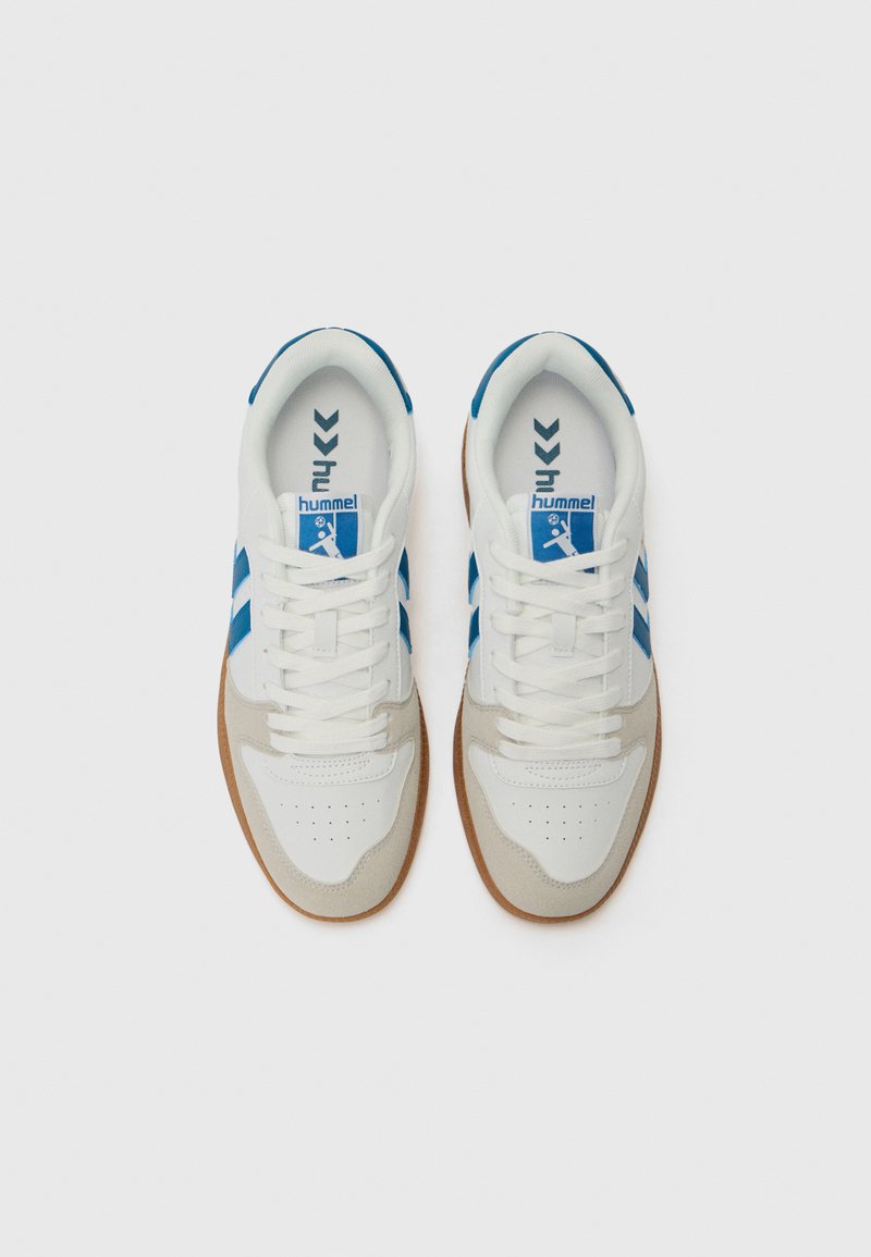 Zapatillas deportivas blancas con acentos azules, con un acabado suave y texturizado, puntera perforada y suela de goma. Dos franjas azules a cada lado.