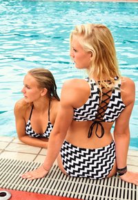 Swimsuits in black and white zigzag pattern; features crisscross back design and contrasting bikini top and bottom styles, shown by two figures.
