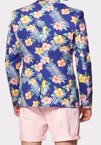 Marynarka w kwiaty w niebieskim kolorze z tropikalnymi kwiatami i liśćmi. Posiada akcenty guzików i dopasowany krój. Połączona z różowymi szortami.
