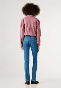 Rødt og hvitt stripete langermet skjorte med knotter på mansjettene, kombinert med blå denimjeans. Synlige baklommer og lærmerke på jeansen.