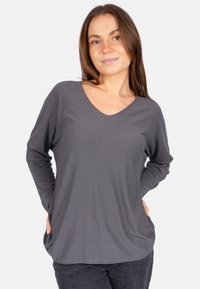 Graues Langarmshirt mit V-Ausschnitt, aus weichem Material gefertigt, mit lässiger Passform und seitlichen Taschen, kombiniert mit dunkelblauen Jeans.
