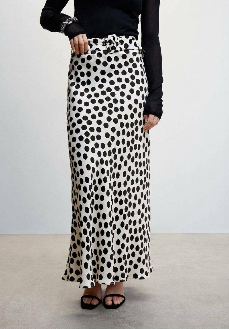 Femme portant un haut noir à manches longues avec une jupe maxi blanche à gros pois noirs et des sandales noires ouvertes à l'avant.
