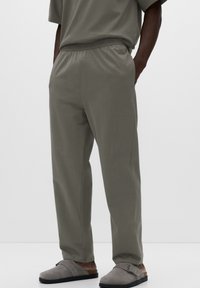 Šedé kalhoty z bavlněné směsi s elastickým pasem, volným střihem a bočními kapsami, v kombinaci se šedými slip-on botami.