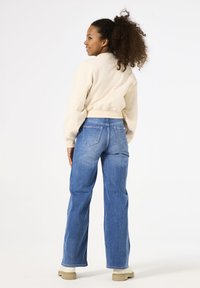 Suéter corto de color beige claro y vaqueros de talle alto azules, con un ajuste relajado y bolsillos traseros visibles. Combinado con zapatos de color claro.
