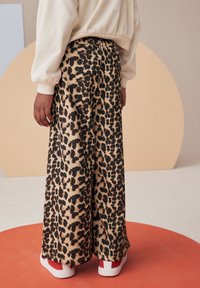 Pantaloni a gamba larga con stampa leopardata in tessuto testurizzato, dotati di vita elastica e abbinati a sneakers con dettagli rossi.