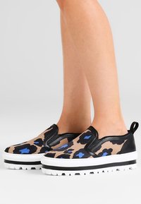 Buciki typu slip-on w nadruk leopardzim, z beżową bazą, czarnymi skórzanymi akcentami i grubą białą gumową podeszwą z teksturowanym bieżnikiem.