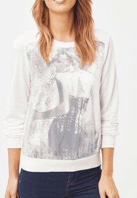 Sudadera blanca de manga larga con una impresión fotográfica translúcida en el frente, que muestra una figura en un corsé.