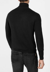 Schwarzer Strick-Pullover mit Rollkragen und langen Ärmeln, mit geripptem Saum, getragen mit dunklen Jeans. Er zeichnet sich durch ein körpernahes Design und eine glatte Textur aus.