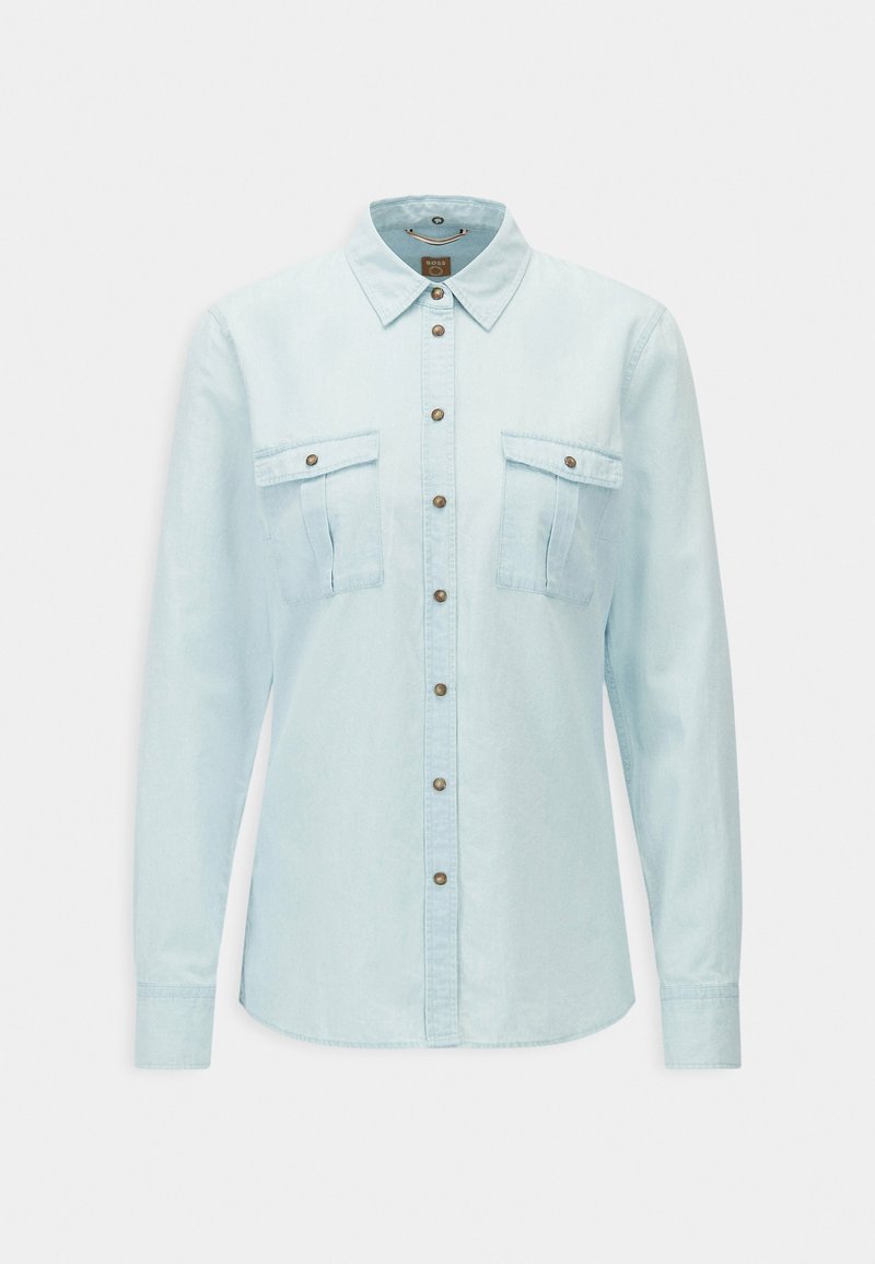 Chemise en denim bleu clair à manches longues, avec fermeture boutonnée sur le devant, col pointu, et deux poches poitrine à rabat boutonné.