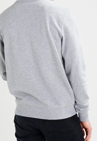 Sudadera gris de manga larga, con cuello y dobladillo acanalados, hecha de una tela suave; combinada con pantalones negros, mostrando la vista trasera.