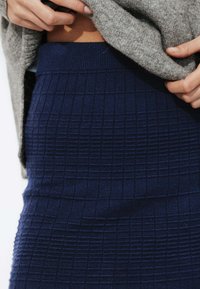 Jupe en maille bleu marine avec un motif en grille texturé, dotée d'une taille côtelée. Superposée sous un pull en maille gris.