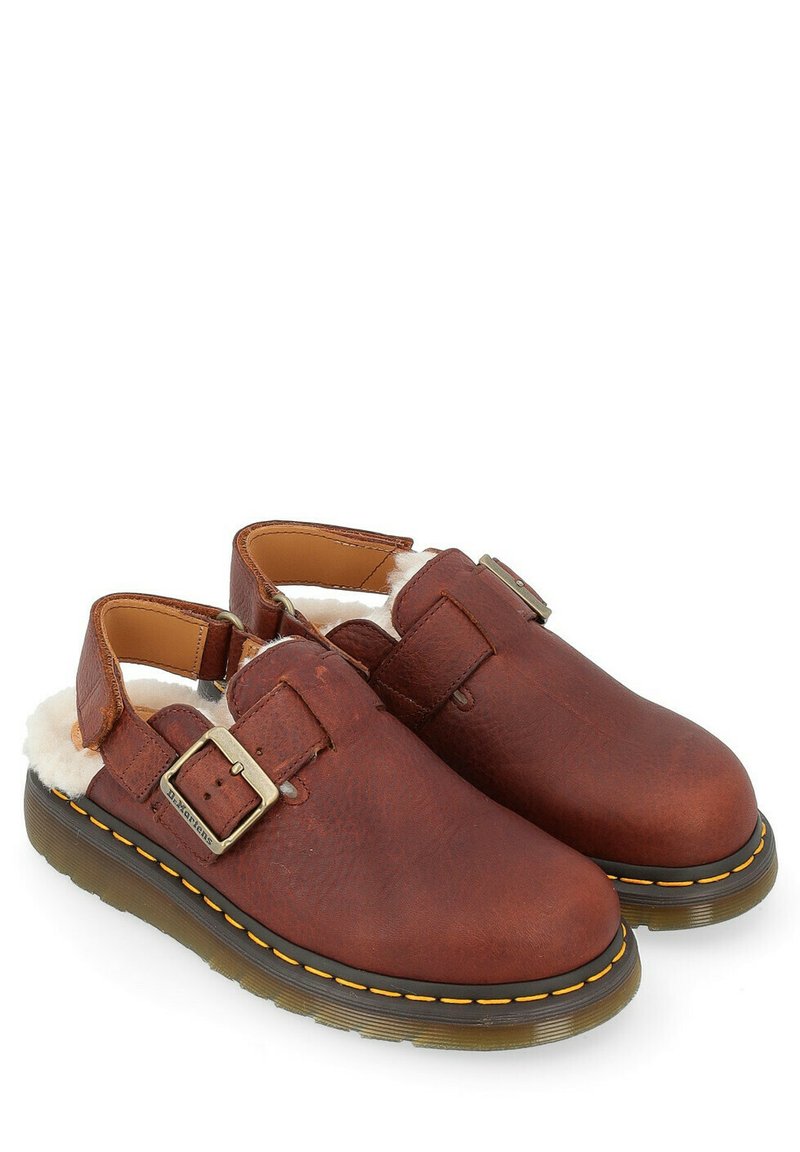 Sabots en cuir marron avec un détail de boucle, intérieure douce en blanc, bout arrondi et semelle en caoutchouc avec des accents de couture jaune.