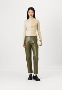 Un pull en col roulé à côtes beige associé à un pantalon en cuir vert. Des chaussures noires à enfiler et un petit sac à main blanc complètent le look.