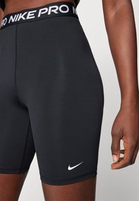 Black Nike Pro compression shorts with a white logo on the lower left. Features a wide, branded waistband and smooth elastic fabric texture.
