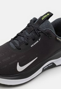 Svart Nike joggesko med teksturert overdel, reflekterende detaljer, grå snøringer og hvit logo. Har en polstret såle for komfort.