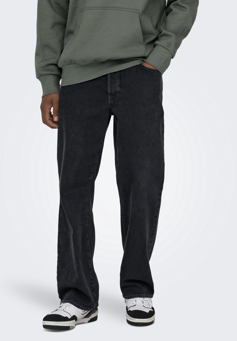 Jean en denim noir coupe décontractée, design à cinq poches avec couture minimaliste, associé à un sweat à capuche gris et des baskets.