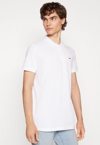 Camisa polo blanca de algodón, con cuello clásico, mangas cortas y un pequeño logotipo en el pecho. Textura suave, ajuste casual.