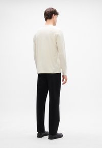 Cămașă lungă bej deschis cu guler rotund, asociată cu pantaloni negri și pantofi slip-on negri. Textură netedă, design minim.