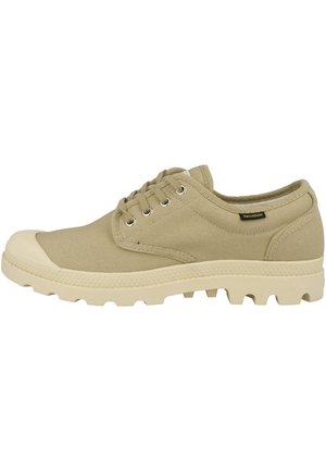 Beige canvas low-top shoe with rubber toe cap, thick textured sole, metal eyelets, and "Palladium" label on the side.
