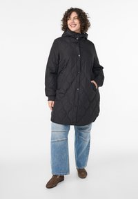 Melnas šūtas virsjaka ar kapuci, poga aizdare un sānu kabatas. Kombinēta ar gaiši zilām platajām džinsa biksēm un brūnām kurpēm.