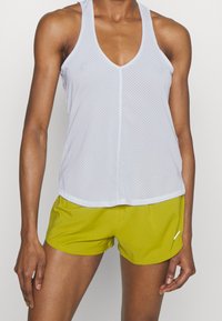 Witte mouwloze mesh tanktop met een V-hals, gecombineerd met felgroene shorts met een klein logo op de zoom. Zachte textuur, relaxte pasvorm.