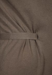 Brunt, texturerat tyg med en rynkad design och ett matchande skärp i midjan för en markerad siluett. Mjukt stickat material.