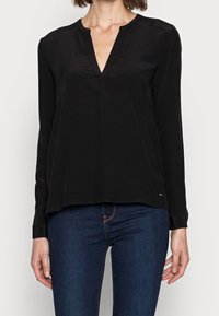 Blusa nera a maniche lunghe con scollatura a V, realizzata in tessuto morbido. Presenta una vestibilità ampia e un piccolo logo accento sull'orlo.
