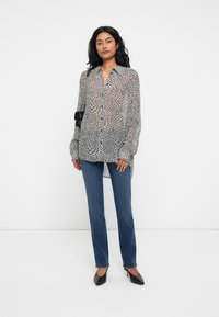 Black and white patterned long-sleeve blouse with button closure, paired with blue jeans and black heels, worn with a small black bag.