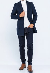 Marinblazer med skräddarsydd passform, två framfickor, kompletterad med en vit ribbad polotröja och mörka jeans. Bruna ankelskängor fulländar looken.