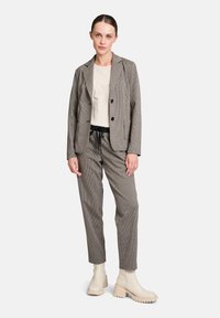 Veste à motifs écossais et pantalon assorti dans des tons de marron, crème et noir. Associé à un haut beige et des bottines couleur crème.