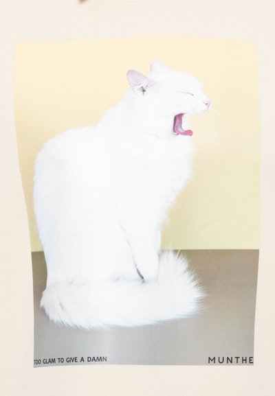 Bela mačka, ki zije, z zaprtimi očmi, puhastim repom in rožnato jezikom na kontrastni rumeni podlagi. Besedilo: "PREVEČ ŠIK, DA BI SE SKRBELI."