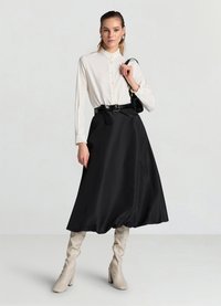 Weiße Bluse mit gerafftem Kragen und Knöpfen, kombiniert mit einem schwarzen Satins-Midirock und beigen kniehohen Stiefeln mit Absatz. Schwarzer Gürtel und Tasche inklusive.