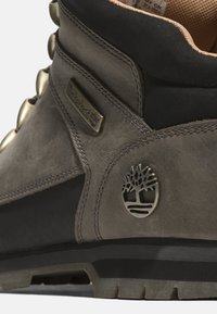 Ciemnoszare skórzane buty z fakturowaną powierzchnią, metalowymi oczkami, czarnym kołnierzem oraz wyraźnym logo drzewka na boku.