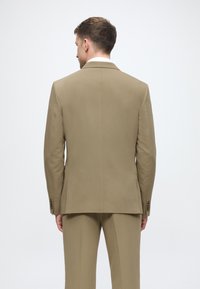 Beiger Blazer von hinten, mit taillierter Passform, glatter Textur, zwei Knöpfen an den Ärmeln und einem eleganten Kragen-Design.