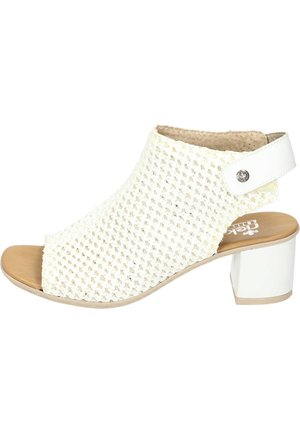 Chaussure à talons blanche ouverte à l'avant avec un dessus tissé, une semelle plate beige et un talon bloc blanc brillant. Présente une sangle latérale avec une clou en argent.