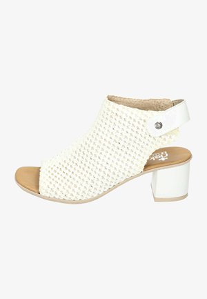 Chaussure à talons blanche ouverte à l'avant avec un dessus tissé, une semelle plate beige et un talon bloc blanc brillant. Présente une sangle latérale avec une clou en argent.