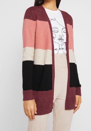 Cardigan avec des couleurs en bloques : bordeaux, rose, beige et noir. Texture douce, ouverture à l'avant, détails côtelés aux poignets et à l'ourlet. Présente un look décontracté.