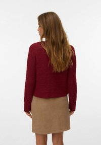 Burgundyröd stickad tröja med texturfinish, kortad nederkant och långa ärmar, matchad med en beige kordbyxor.