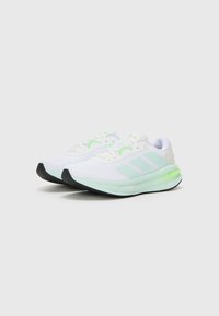 Zapatillas deportivas blancas con parte superior de malla texturizada, acentos en verde menta, logotipo de tres rayas y suela de goma negra.