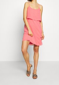 Rosa ärmelloses Kleid mit geschichtetem Design, aus weichem Stoff gefertigt. Hat einen lockeren Schnitt und eine subtile Textur, kombiniert mit Sandalen im Leopardenmuster.