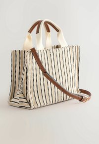 Sac fourre-tout rayé avec un mélange de matériaux tissés crème et noir, doté de poignées en cuir marron et d'une bandoulière amovible.