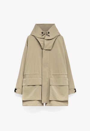 Veste légère beige avec un col haut, de grandes poches avant et une fermeture éclair. Présente une coupe décontractée et oversize avec une texture douce.